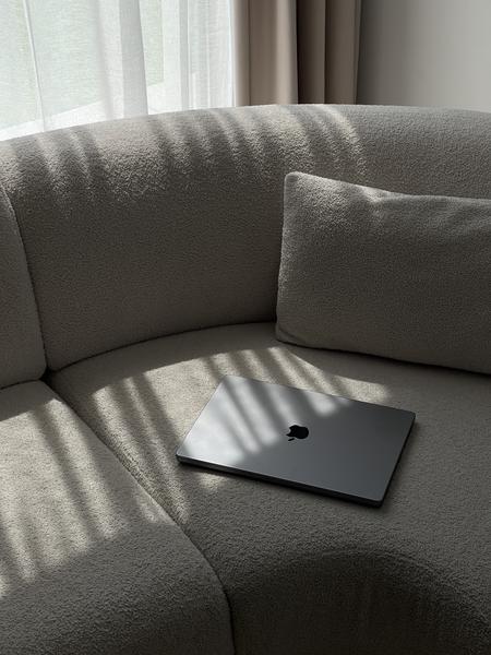 A Macbook sitting on a couch in the sun.